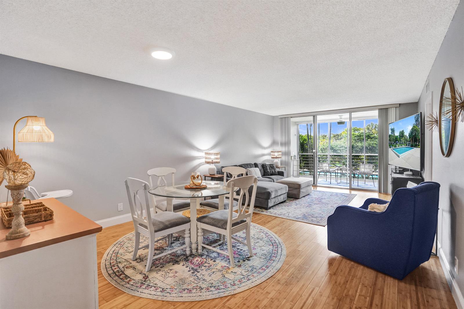 A living and dining area features a glass table, gray sectional, blue armchair, and balcony — 4200 Oaks Terrace # 203, Pompano Beach FL 33069, POMPANO BEACH, FL