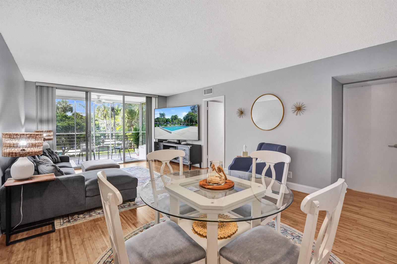 A living and dining area features a grey sectional, glass-topped table, and sliding balcony doors — 4200 Oaks Terrace # 203, Pompano Beach FL 33069, POMPANO BEACH, FL