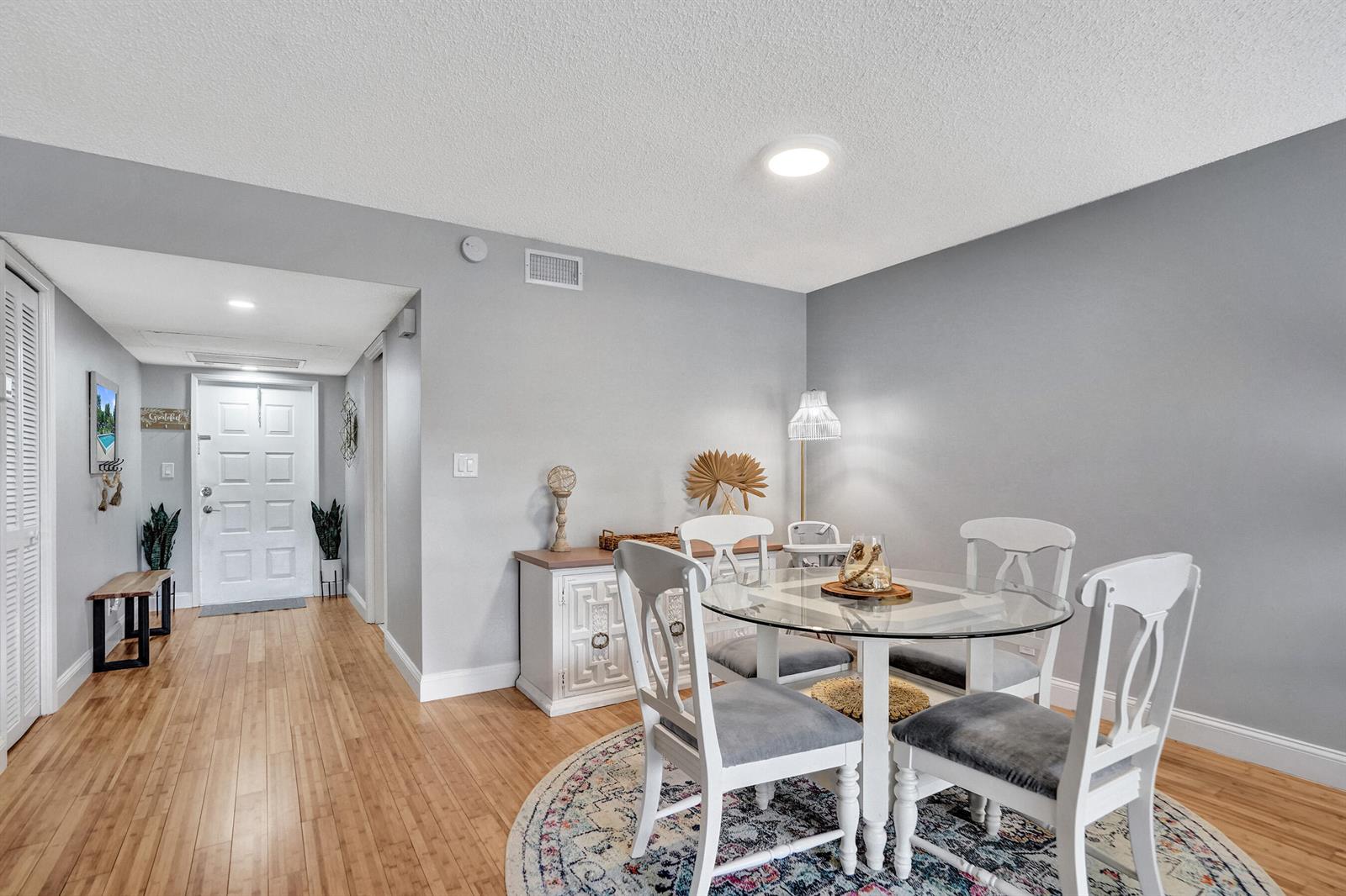 A dining area with a glass-topped table and white chairs sits on a patterned rug — 4200 Oaks Terrace # 203, Pompano Beach FL 33069, POMPANO BEACH, FL