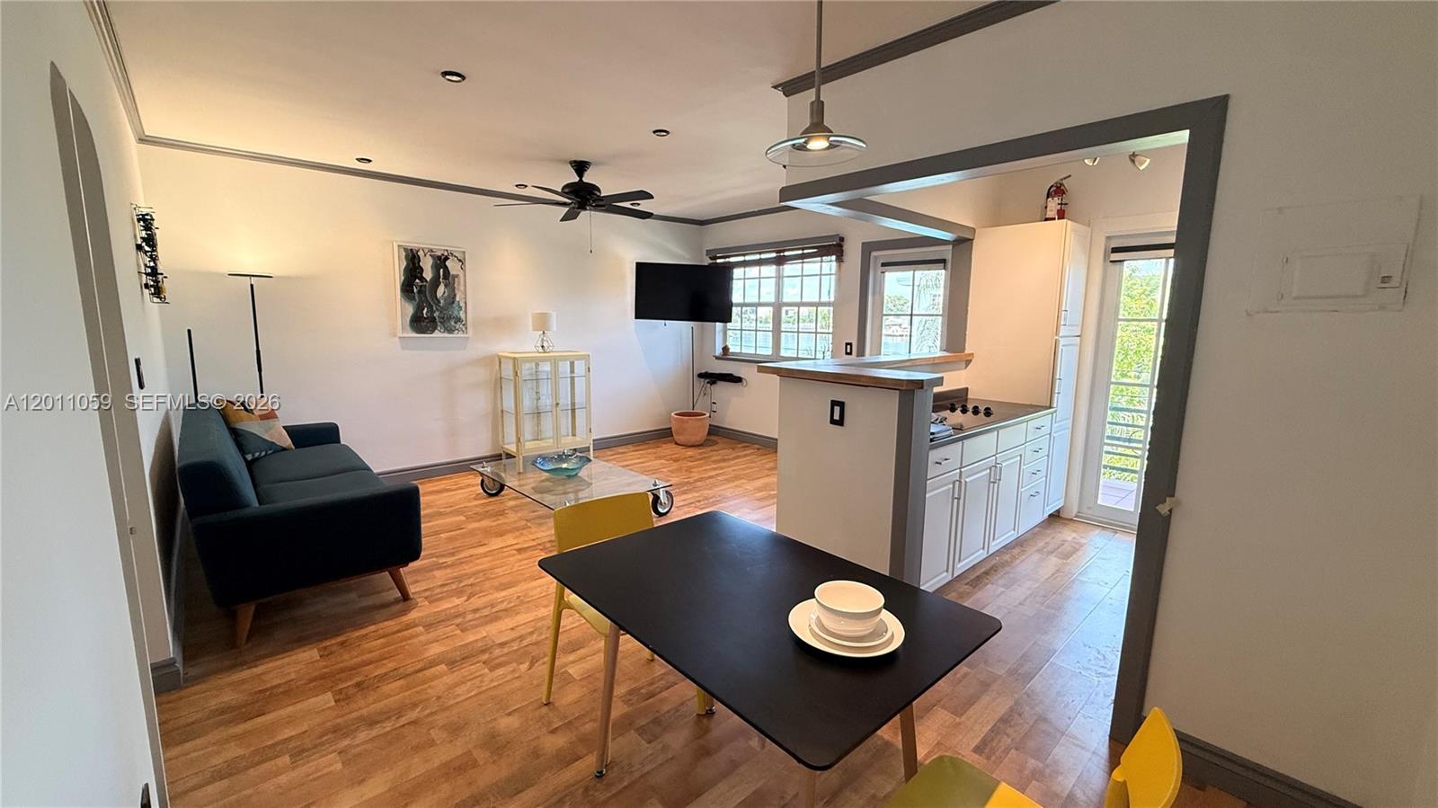 An open-concept living and dining area features wood-look flooring, white walls, and a small kitchen — 8600 Byron Ave # 8, Miami Beach FL 33141, MIAMI BEACH, FL