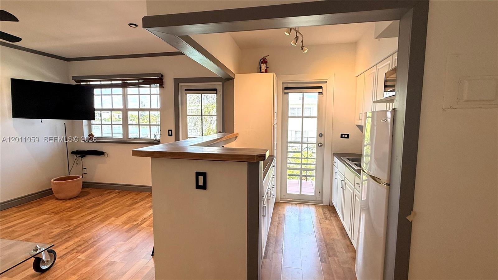 A kitchen with white cabinets and a breakfast bar opens into a living area — 8600 Byron Ave # 8, Miami Beach FL 33141, MIAMI BEACH, FL