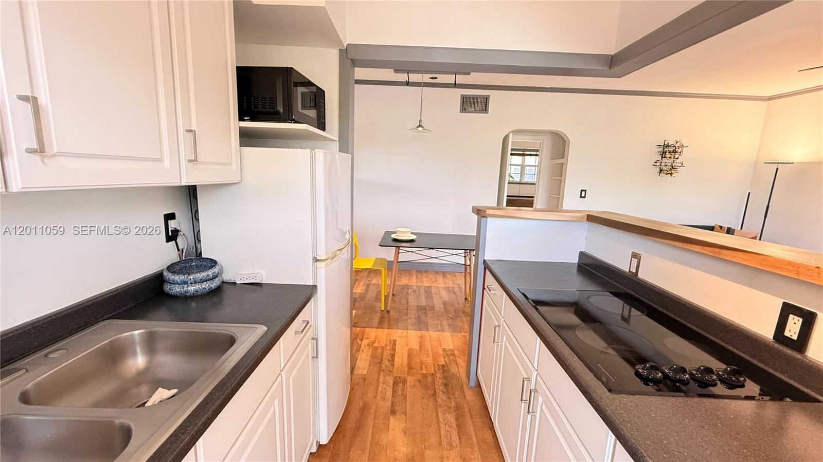 A kitchen with white cabinets, dark countertops, and a stainless steel sink overlooks a dining area — 8600 Byron Ave # 8, Miami Beach FL 33141, MIAMI BEACH, FL