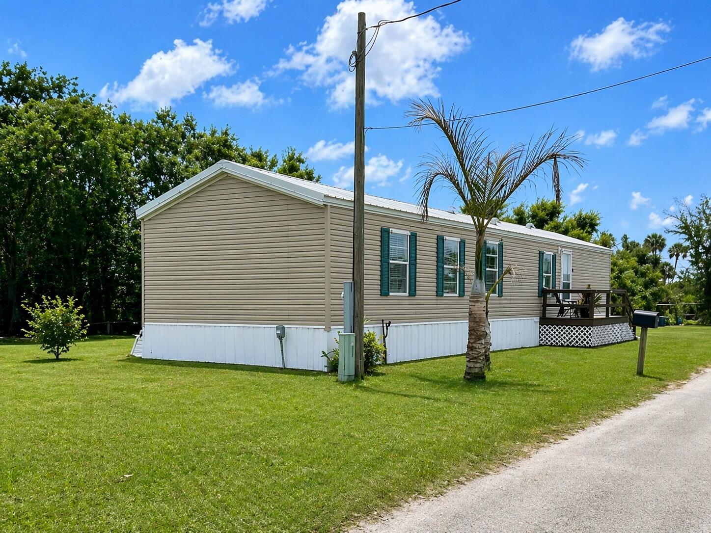 A tan mobile home with white skirting and green shutters sits on a grassy lot — 1905 SE 8th Avenue, Okeechobee FL 34974, OKEECHOBEE, FL