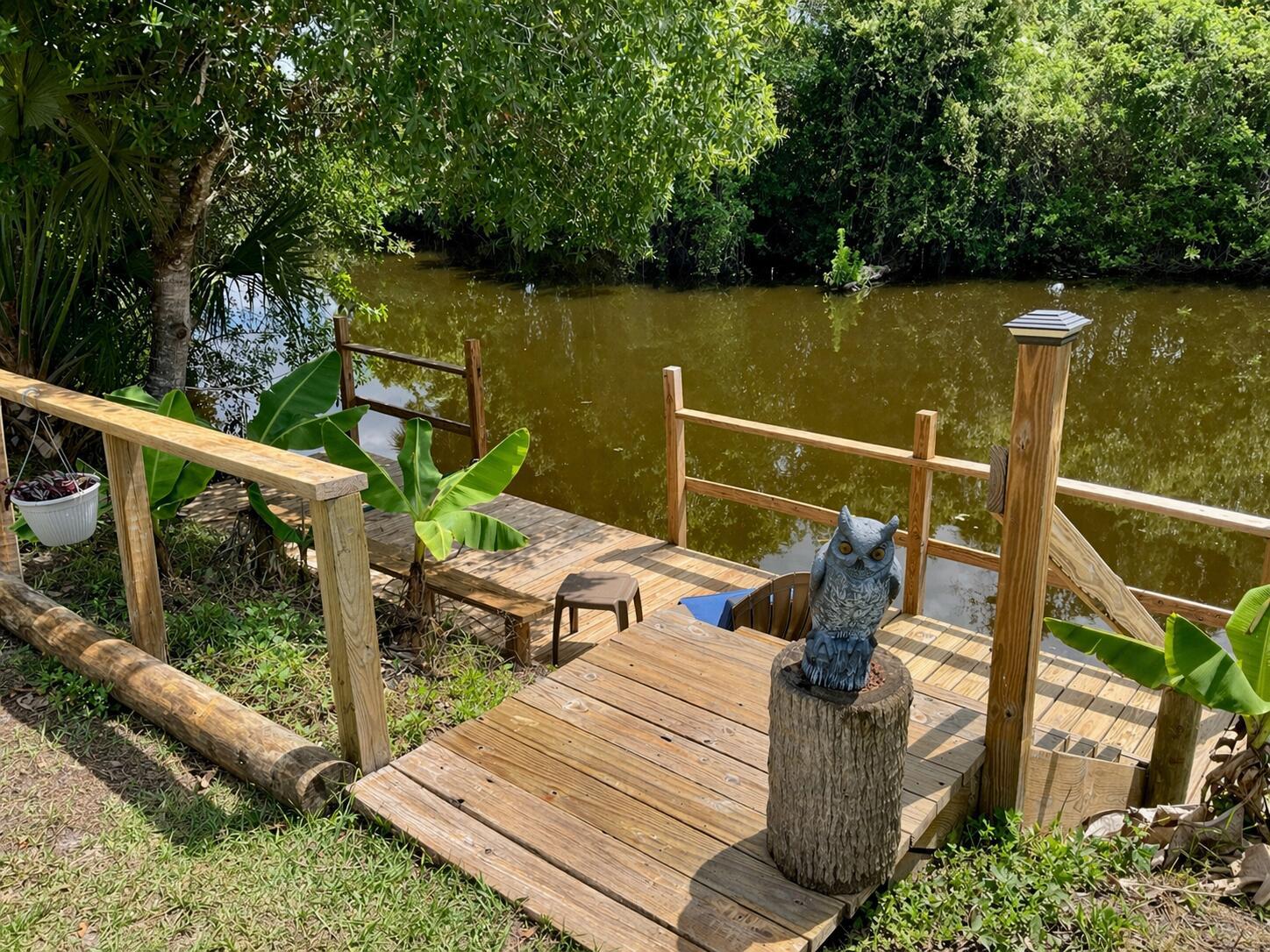 A wooden deck with a railing and an owl statue overlooks a calm, murky canal — 1905 SE 8th Avenue, Okeechobee FL 34974, OKEECHOBEE, FL