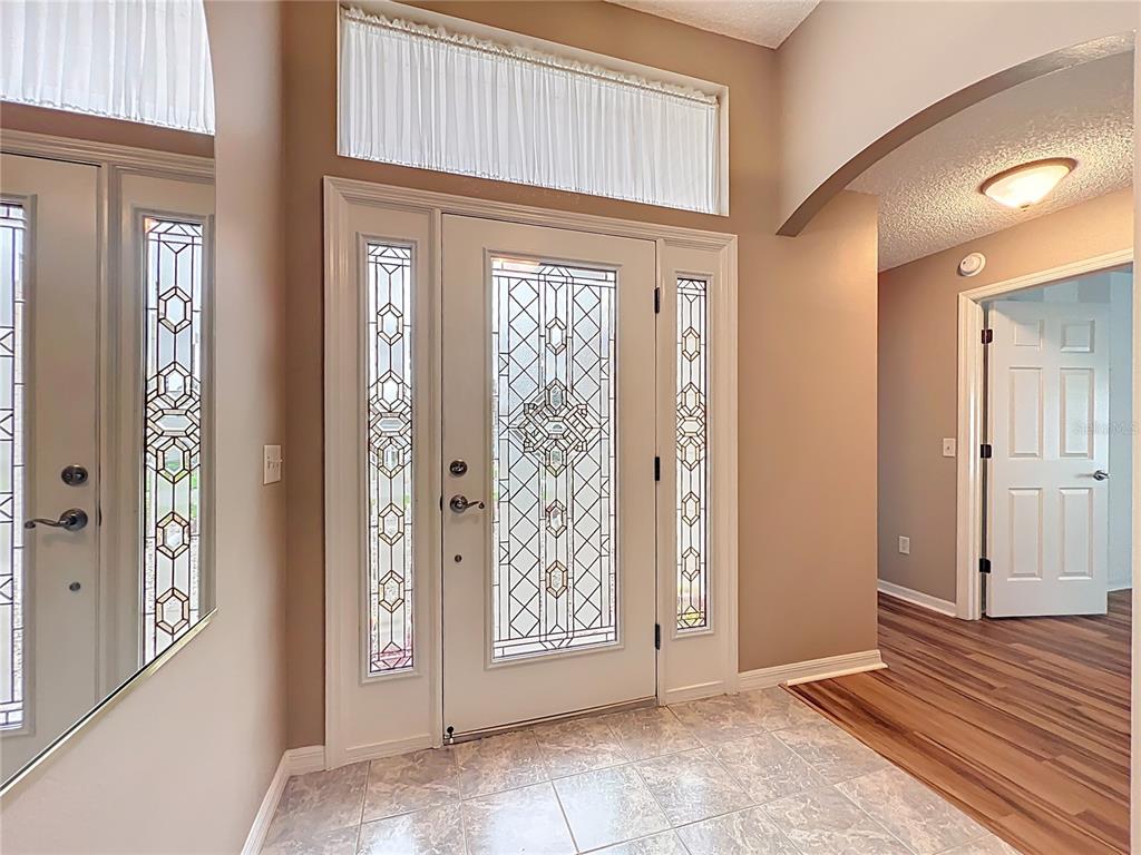 An entryway features a decorative glass front door with sidelights, tile flooring, and wood-look flooring — 16946 SE 93RD CUTHBERT CIRCLE, THE VILLAGES, FL