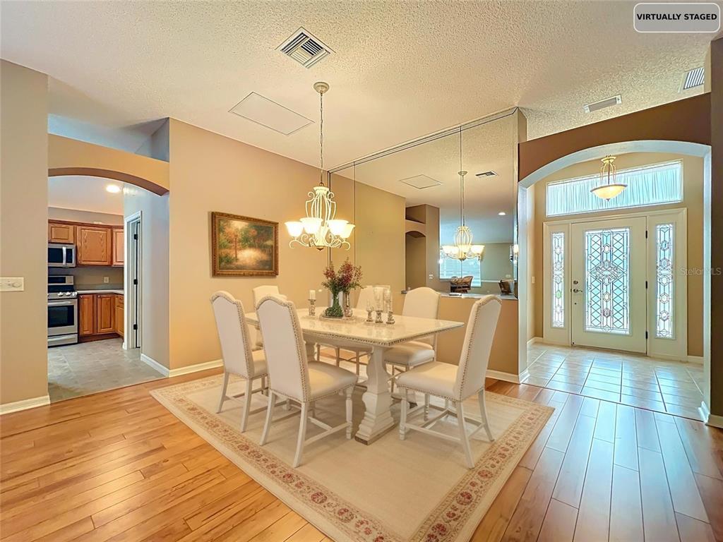 A dining room with a white table, upholstered chairs, a mirrored wall, and hardwood floors — 16946 SE 93RD CUTHBERT CIRCLE, THE VILLAGES, FL