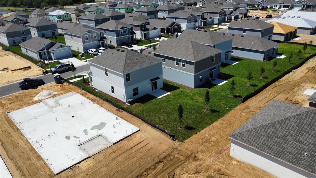 An aerial view shows a suburban neighborhood with completed houses and a concrete foundation slab — 441 SANDBAR LANE, HAINES CITY, FL