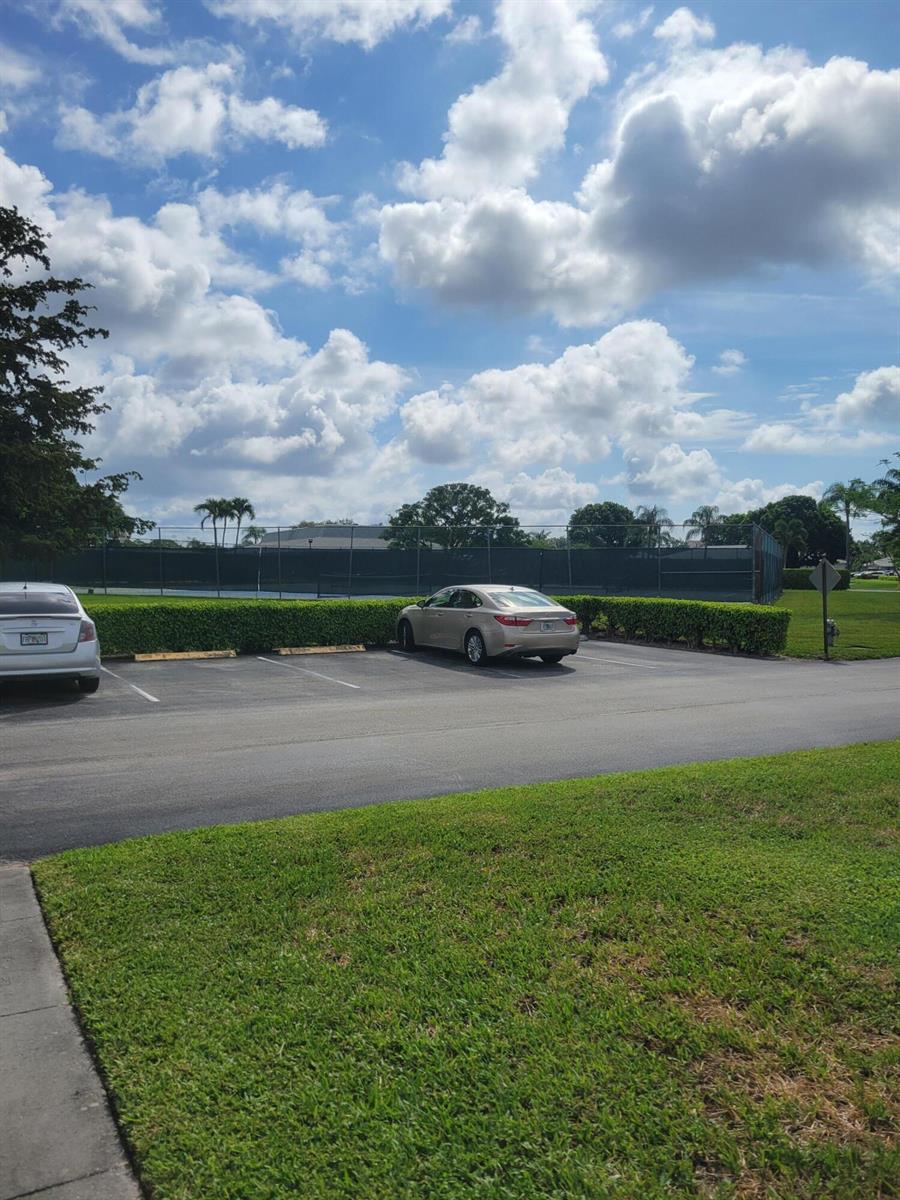A parking lot with two cars parked in front of a fenced tennis court — 14629 Canalview Drive # C, Delray Beach FL 33484, DELRAY BEACH, FL