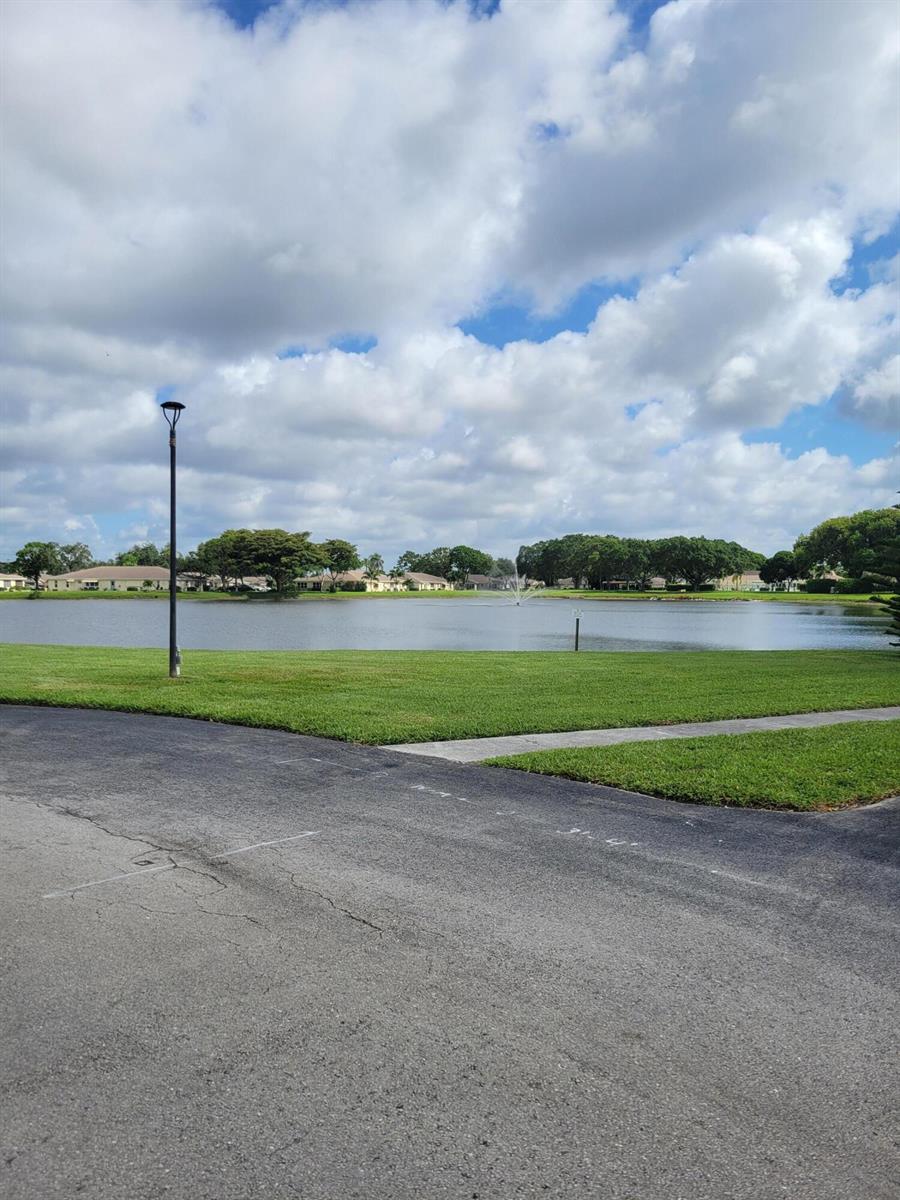 A view of a lake with a fountain, surrounded by green grass and residential homes — 14629 Canalview Drive # C, Delray Beach FL 33484, DELRAY BEACH, FL
