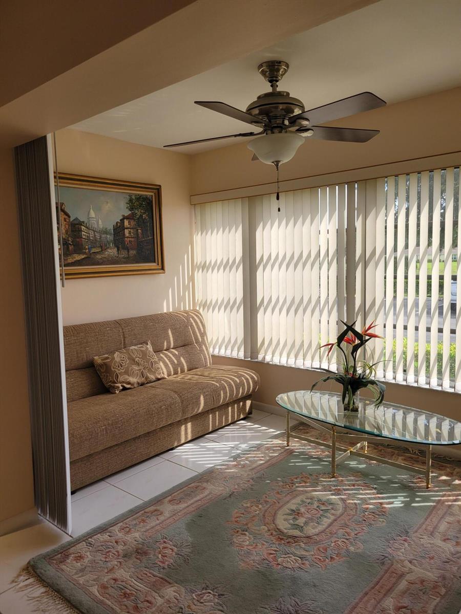 A sunroom features a beige sofa, a glass coffee table, a rug, and vertical blinds — 14629 Canalview Drive # C, Delray Beach FL 33484, DELRAY BEACH, FL