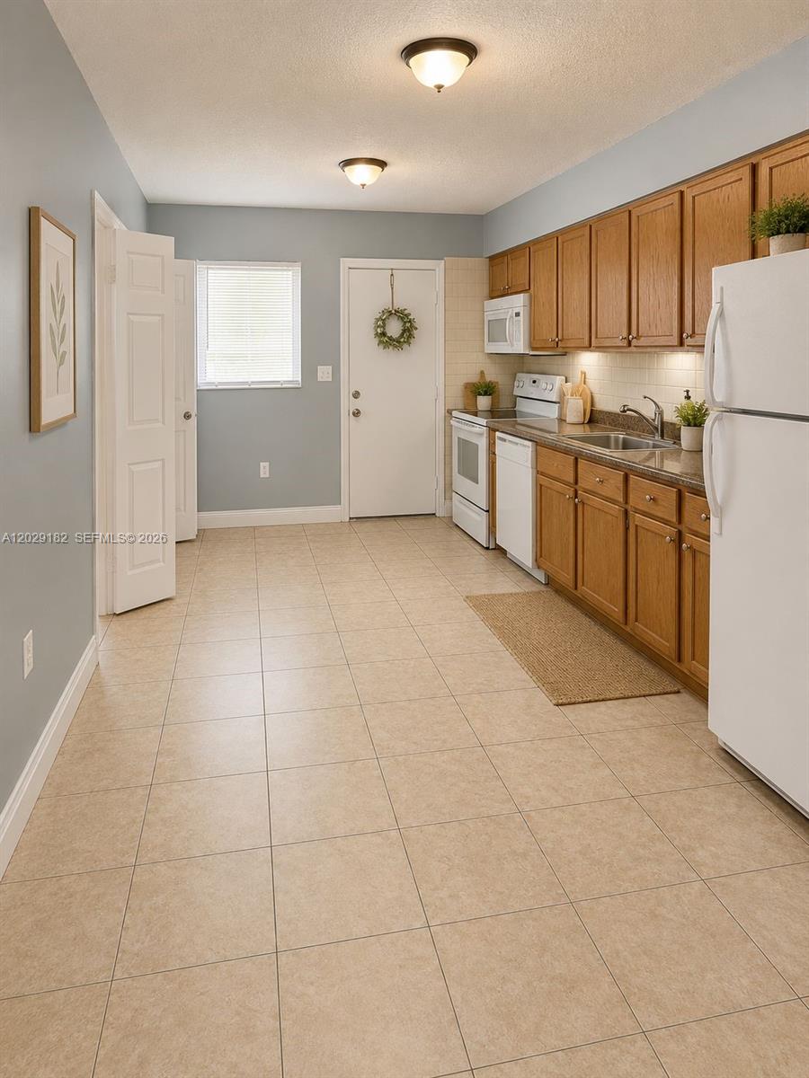 A kitchen features light-colored tile flooring, wood cabinets, white appliances, and light blue walls — 701 SW 1st St # 1, Dania Beach FL 33004, DANIA BEACH, FL