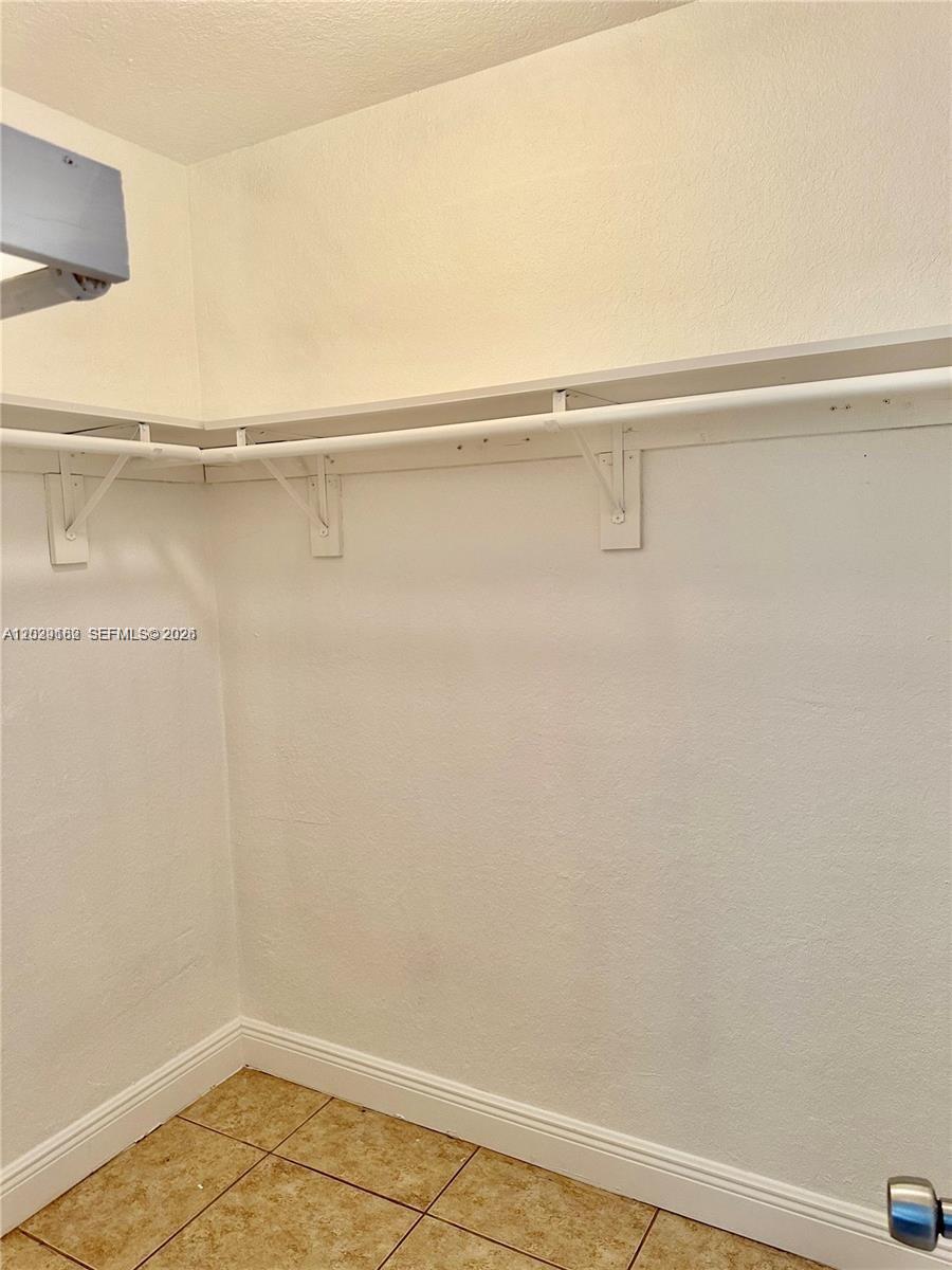 A walk-in closet features white walls, a shelf with a hanging rod, and tiled flooring — 701 SW 1st St # 1, Dania Beach FL 33004, DANIA BEACH, FL