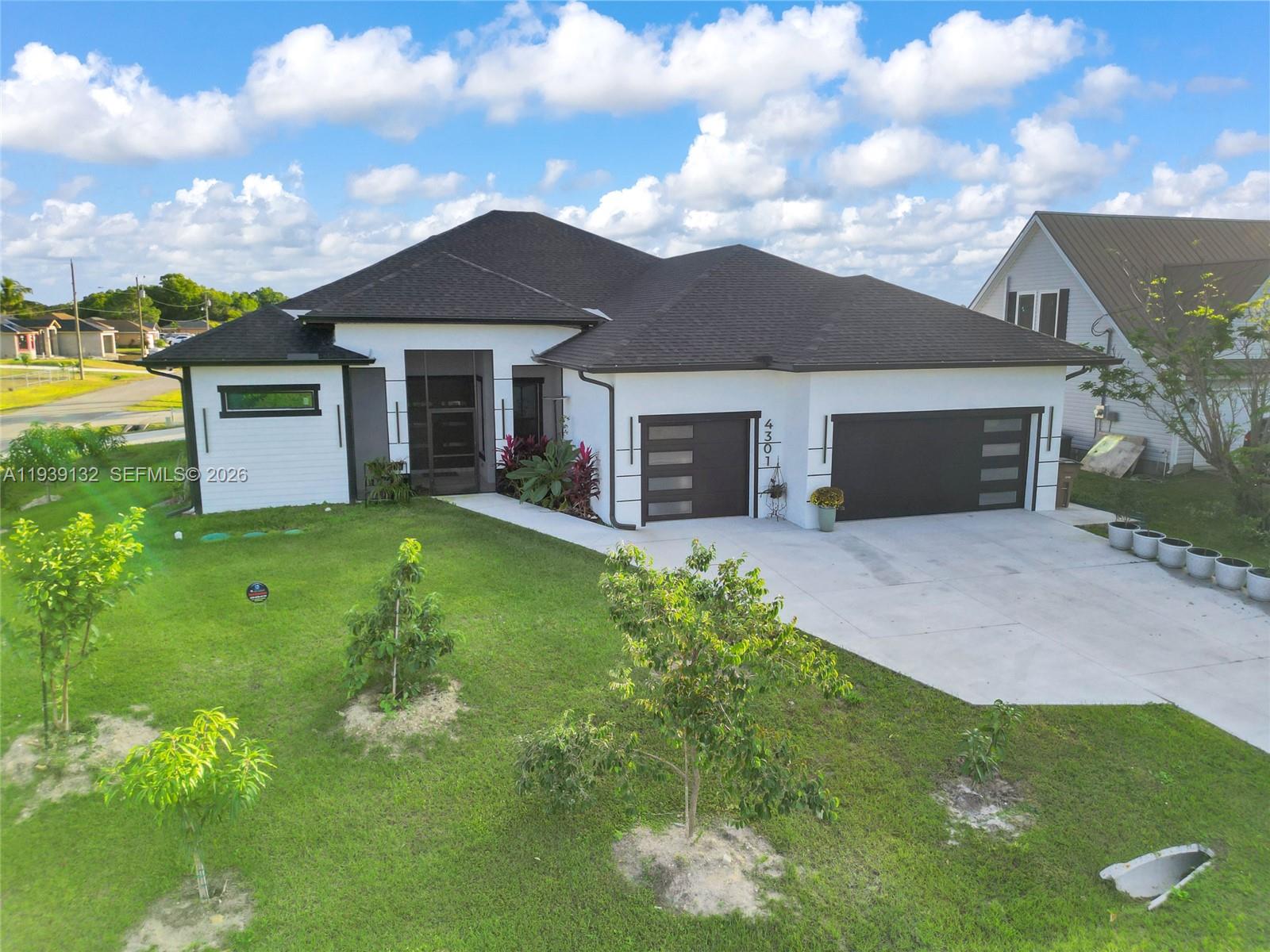 An aerial view shows a modern white house with a dark roof and three-car garage — 4301 10th ST W, Lehigh Acres FL 33971, LEHIGH ACRES, FL