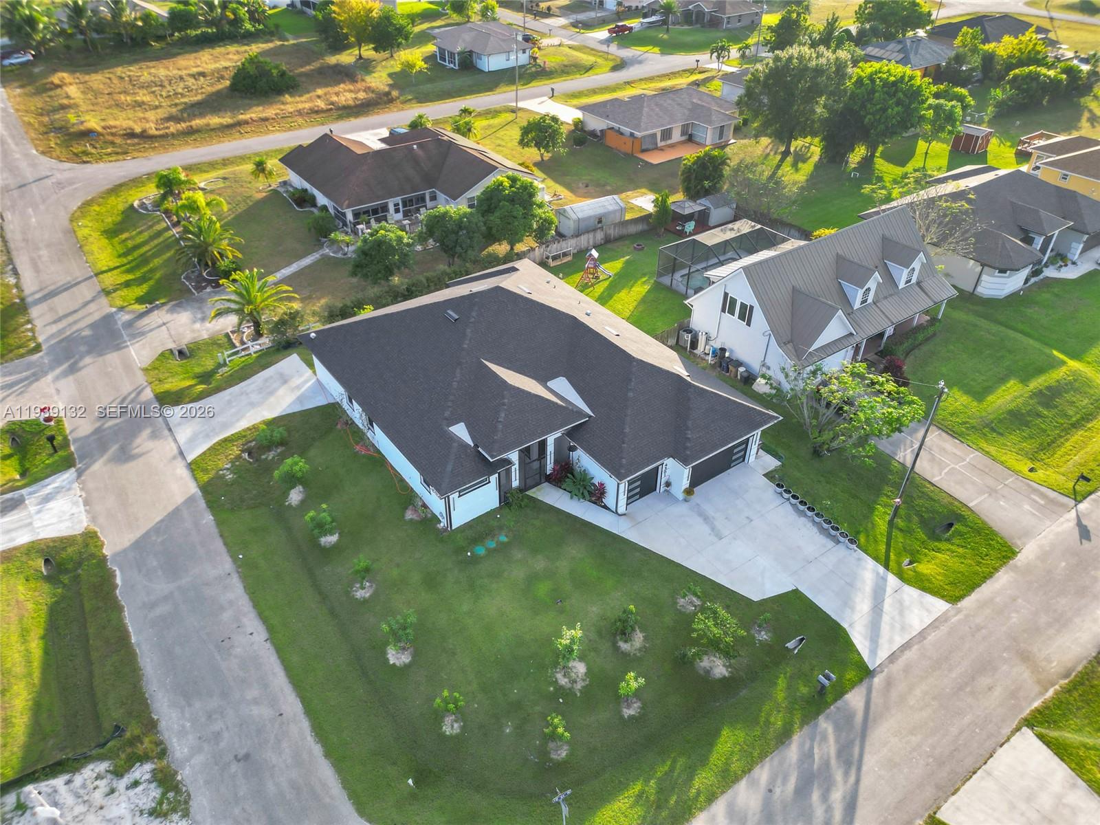 An aerial view shows a suburban house with a dark roof and a concrete driveway — 4301 10th ST W, Lehigh Acres FL 33971, LEHIGH ACRES, FL