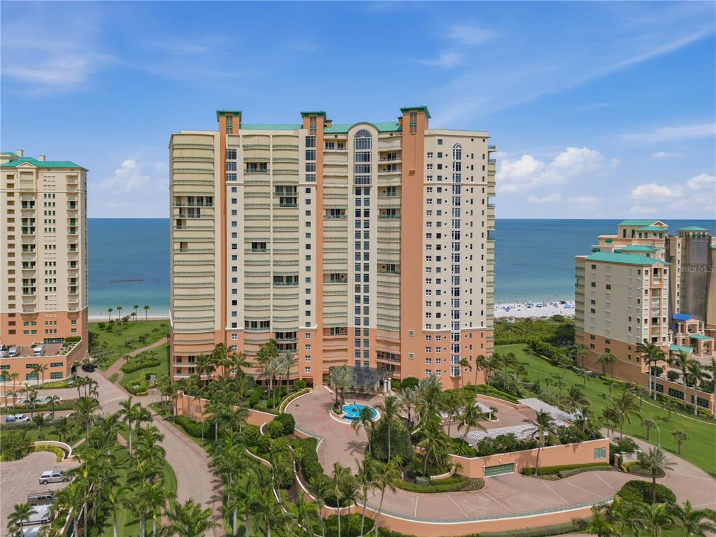 An aerial view shows a large beachfront condominium complex with palm trees and a circular driveway — 940 CAPE MARCO DRIVE UNIT 1905, MARCO ISLAND, FL