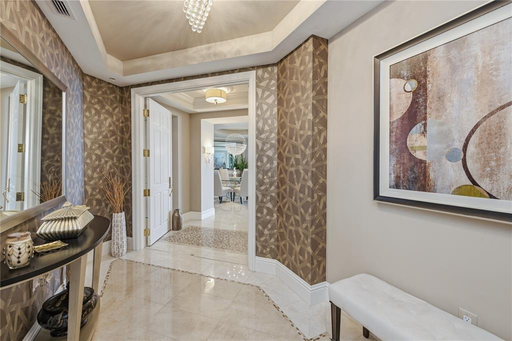 A foyer features patterned wallpaper, a console table, a bench, and a view into a dining area — 940 CAPE MARCO DRIVE UNIT 1905, MARCO ISLAND, FL
