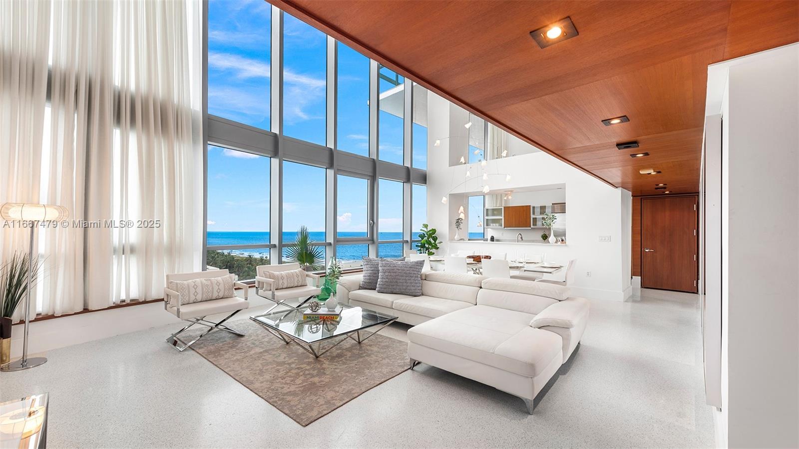 A modern living room features floor-to-ceiling windows with ocean views and a wood-paneled ceiling — 101 20th St Th B # 1505, Miami Beach FL 33139, MIAMI BEACH, FL