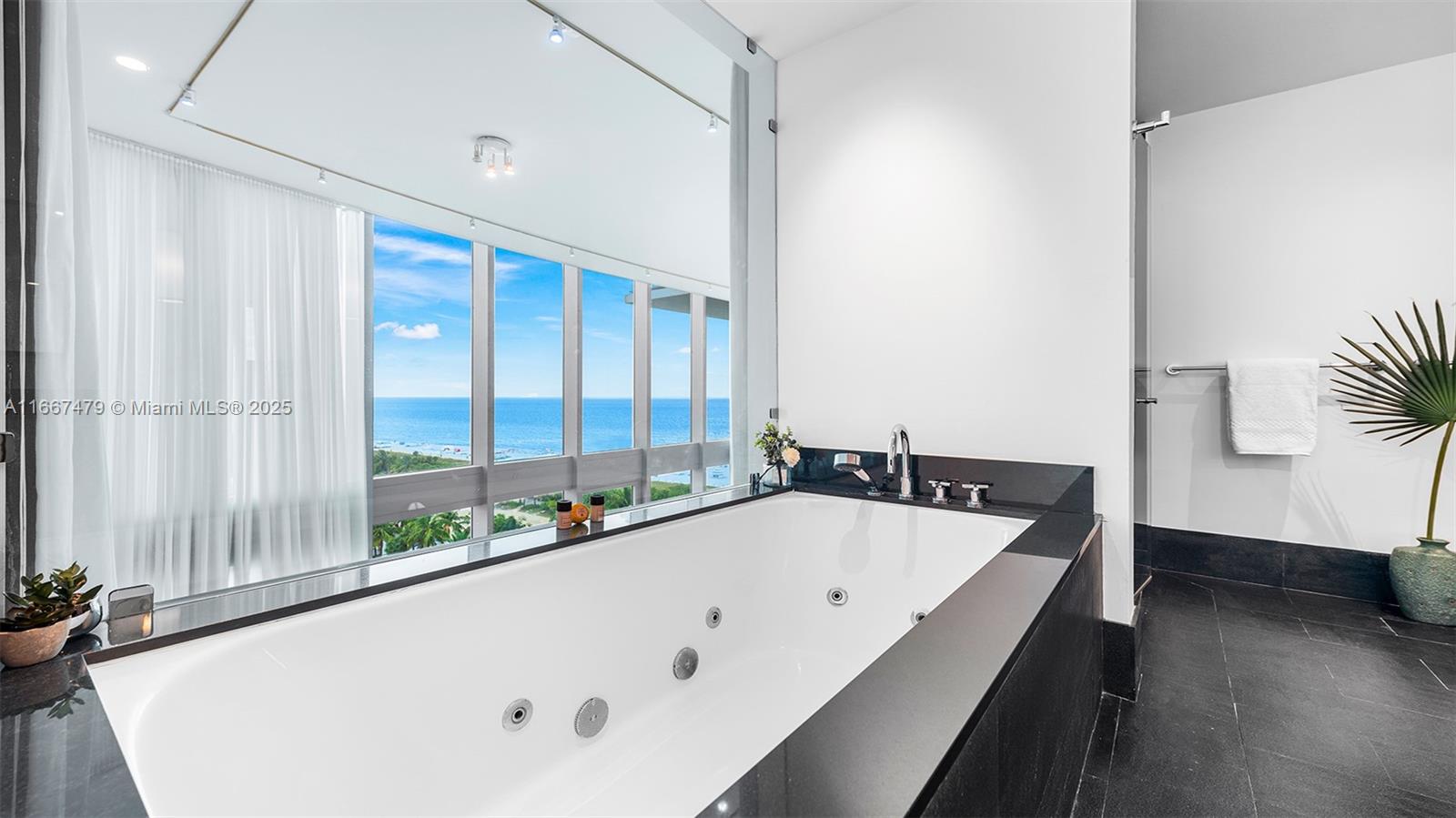 A white jetted bathtub sits against a black stone deck with floor-to-ceiling ocean views — 101 20th St Th B # 1505, Miami Beach FL 33139, MIAMI BEACH, FL