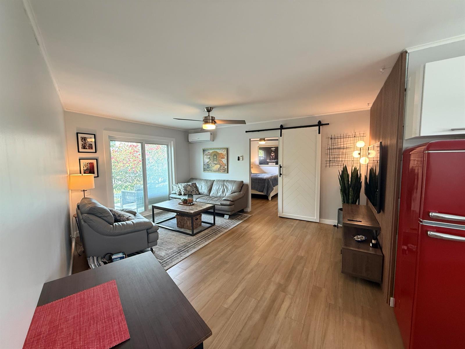 A living room features light wood flooring, a gray sofa, a sliding barn door, and a refrigerator — 203 Seacrest Lane # A, Delray Beach FL 33444, DELRAY BEACH, FL