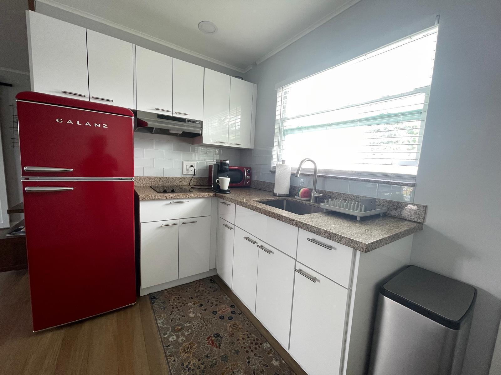 A small kitchen features white cabinets, granite countertops, and a bright red Galanz refrigerator — 203 Seacrest Lane # A, Delray Beach FL 33444, DELRAY BEACH, FL