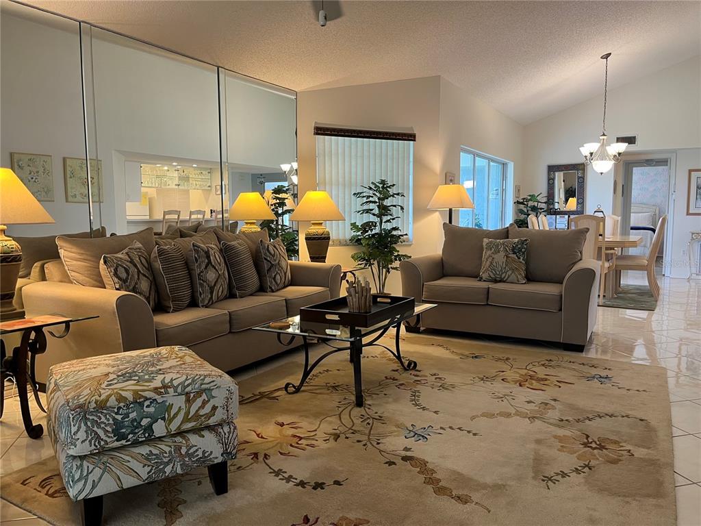 A living room features beige sofas, a patterned ottoman, a glass coffee table, and mirrors — 1397 PERICO POINT CIRCLE UNIT 1397, BRADENTON, FL