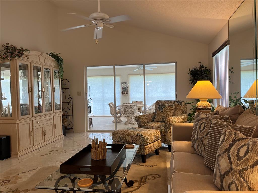 A living room features a glass coffee table, patterned armchair with ottoman, and sliding glass doors — 1397 PERICO POINT CIRCLE UNIT 1397, BRADENTON, FL