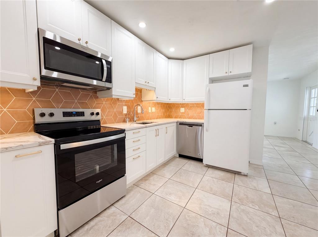 A kitchen with white cabinets, stainless steel appliances, and a geometric orange tile backsplash — 829 E 4TH STREET, ENGLEWOOD, FL
