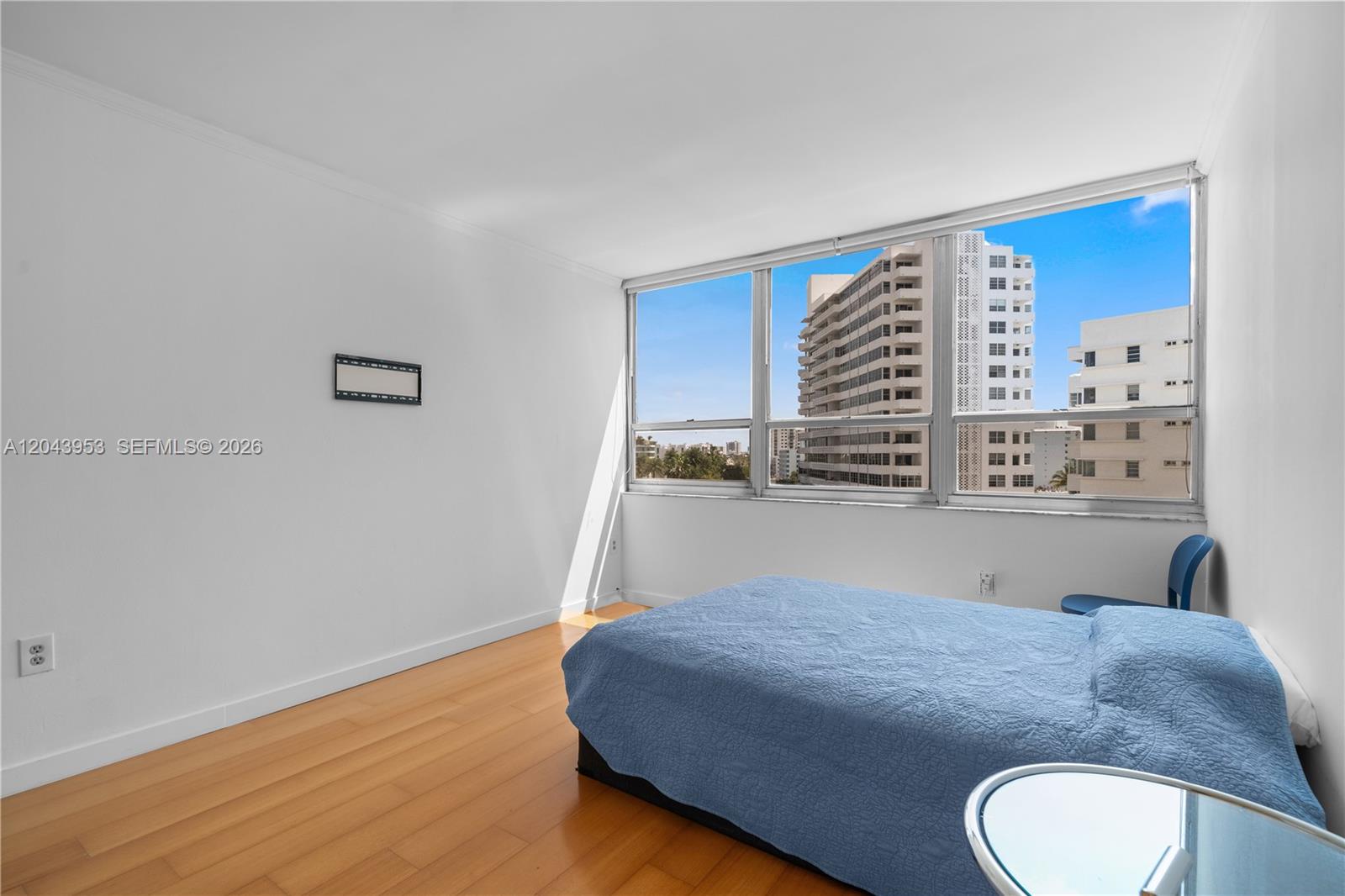 A bedroom with light wood flooring, a blue bed, and large windows overlooking city buildings — 11 Island Ave # 610, Miami Beach FL 33139, MIAMI BEACH, FL