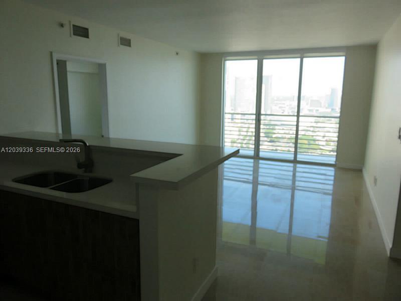 A kitchen island with a double sink overlooks a living area with floor-to-ceiling windows — 325 S BISCAYNE BLVD # 4122, Miami FL 33131, MIAMI, FL