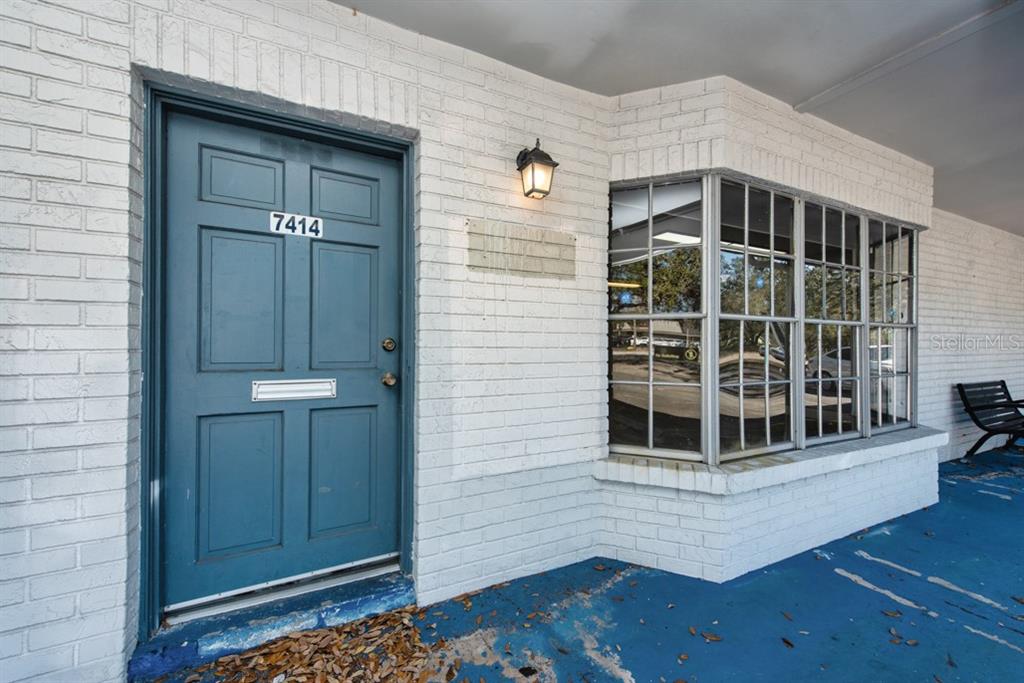 A blue door with the number 7414 sits beside a large window on a brick building — 7414 COMMERCE STREET UNIT 102, RIVERVIEW, FL
