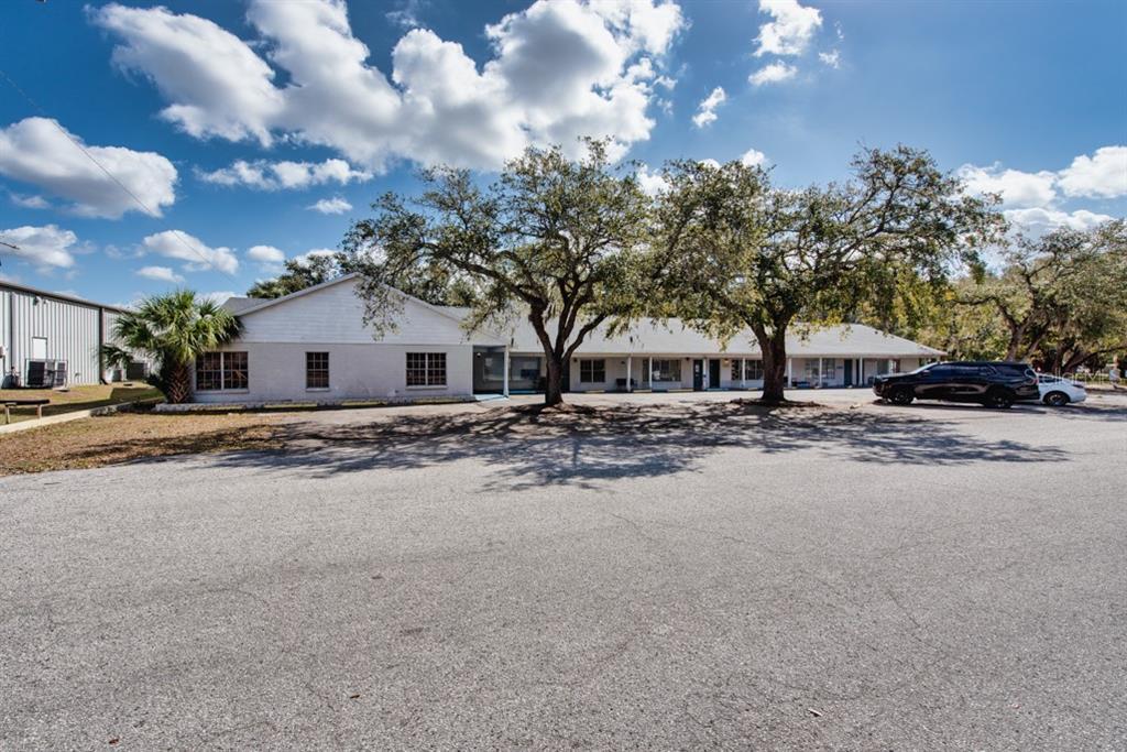 A single-story commercial building with a large parking lot and mature trees in front — 7414 COMMERCE STREET UNIT 102, RIVERVIEW, FL