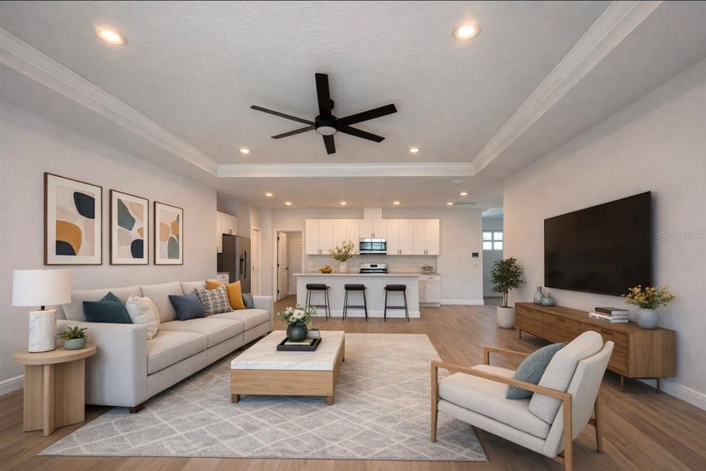 A living room with a tray ceiling, light wood floors, and an open kitchen beyond — 131 KINGS DRIVE, ROTONDA WEST, FL