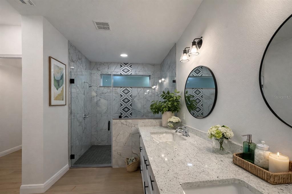 A modern bathroom features a glass-enclosed shower, marble-look tile, dual sinks, and round mirrors — 131 KINGS DRIVE, ROTONDA WEST, FL
