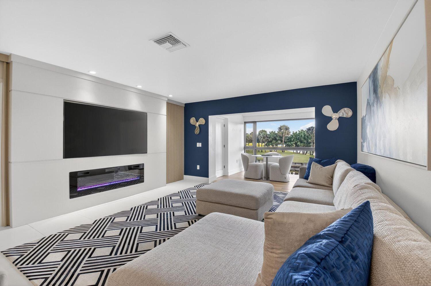 A modern living room features a large sectional sofa, a fireplace, and a blue accent wall — 23 Southport Lane # D, Boynton Beach FL 33436, BOYNTON BEACH, FL