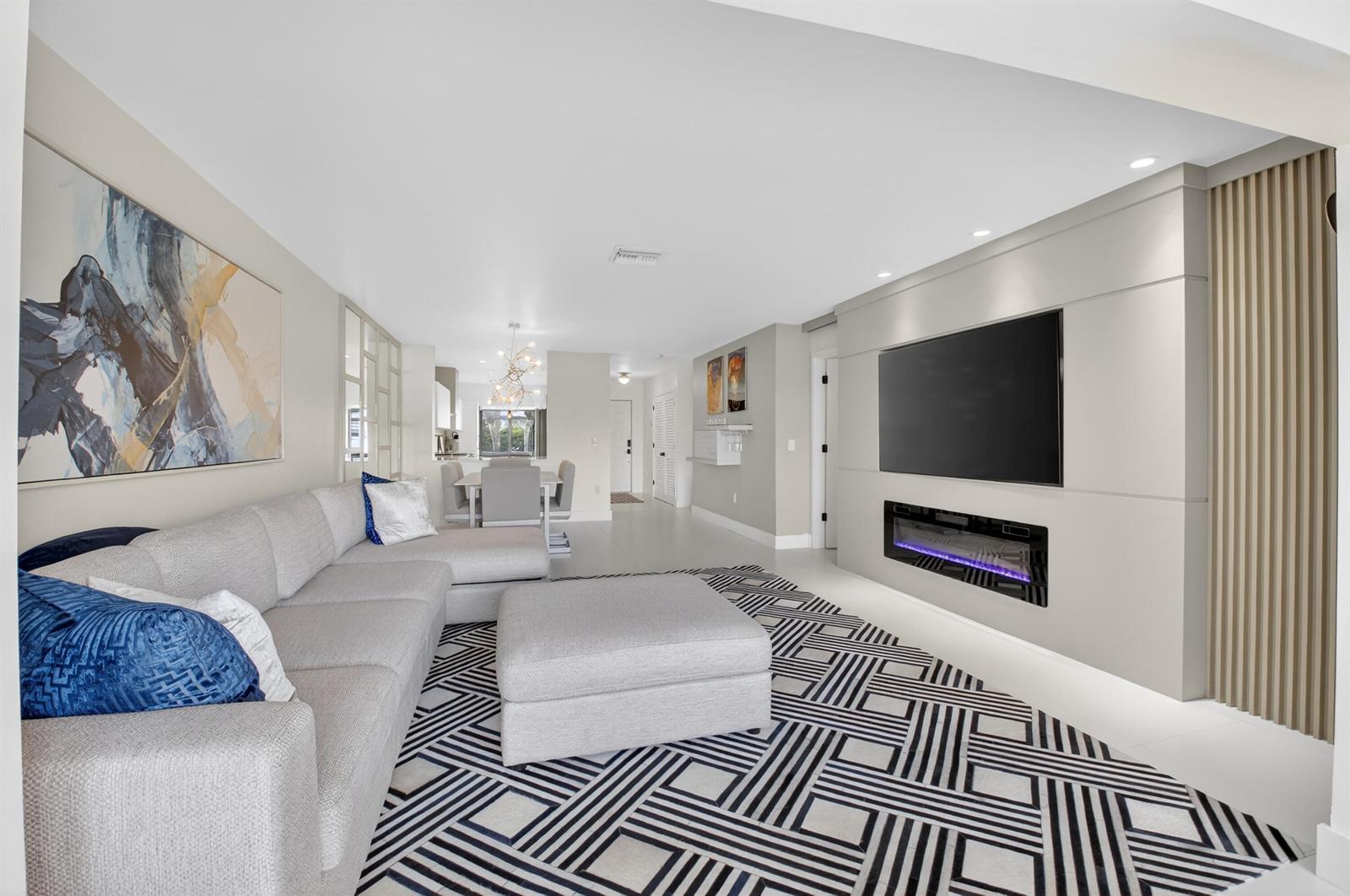 A living room features a grey sectional sofa, a patterned rug, and a wall-mounted television — 23 Southport Lane # D, Boynton Beach FL 33436, BOYNTON BEACH, FL