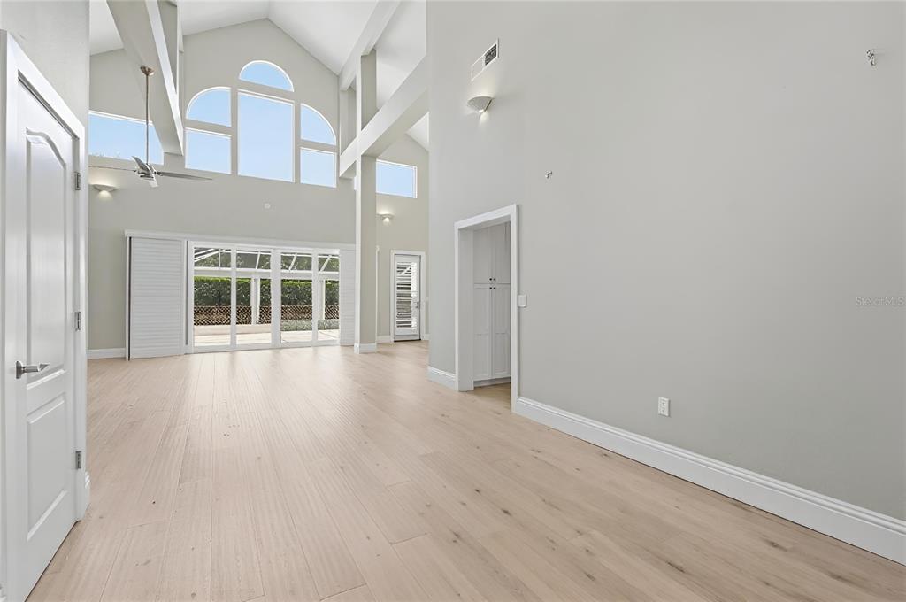 A spacious, high-ceilinged living room features light wood floors, large arched windows, and white walls — 1511 N LAKE SHORE DRIVE, SARASOTA, FL