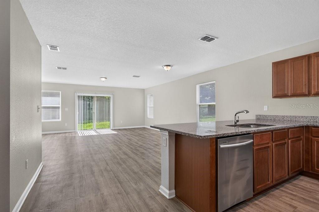 A kitchen with granite countertops and stainless steel appliances overlooks an open living area — 7082 PLYMOUTH GROVE COURT, JACKSONVILLE, FL