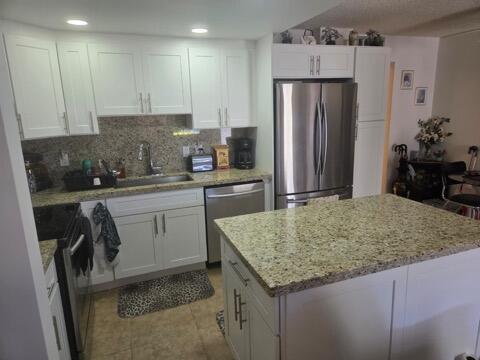 A kitchen features white cabinetry, granite countertops, a stainless steel refrigerator, and a center island — 188 Grantham F # 188, Deerfield Beach FL 33442, DEERFIELD BEACH, FL