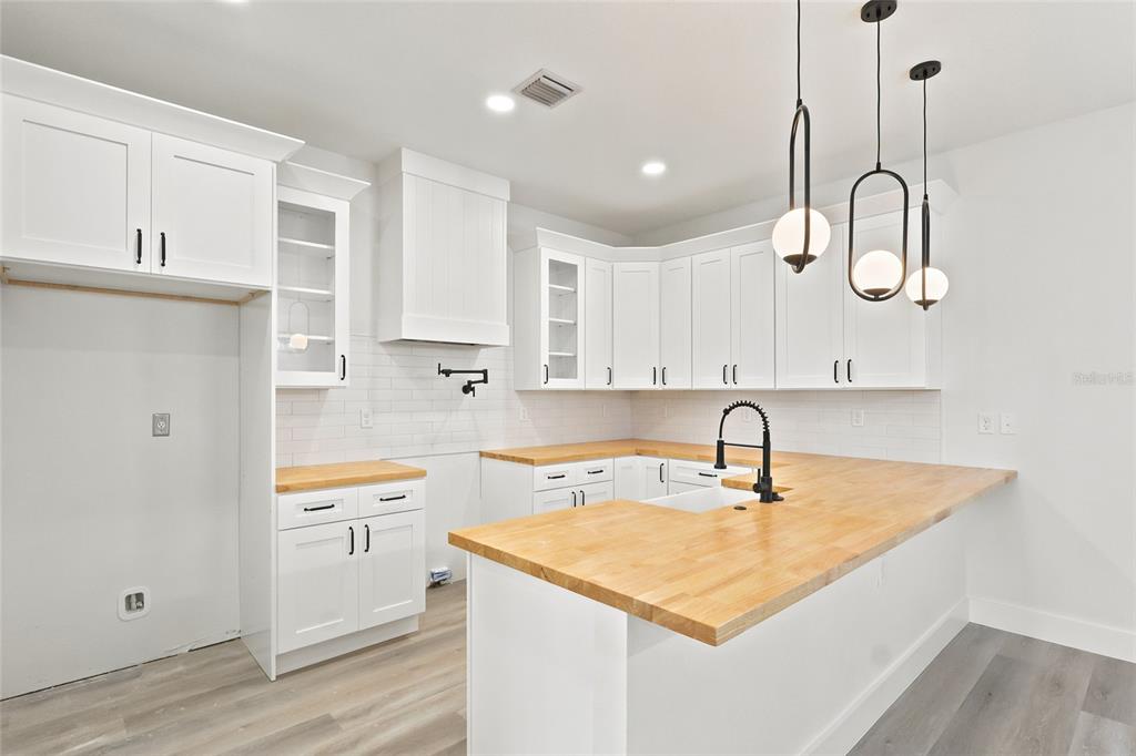 A modern kitchen features white cabinets, butcher block countertops, a farmhouse sink, and pendant lighting — 2138 W NASSAU STREET UNIT 2, TAMPA, FL