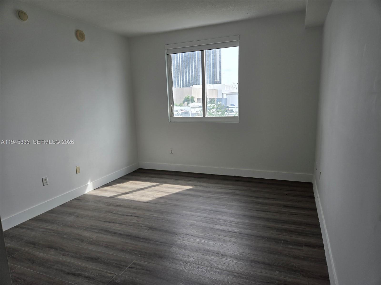 An empty room features white walls, dark wood-look flooring, and a single window — 275 NE 18th St # 503, Miami FL 33132, MIAMI, FL