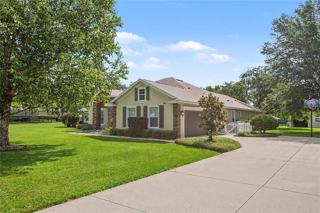 A single-story house with a tan exterior, stone accents, and a large concrete driveway — 12913 COUNTY ROAD 104B, OXFORD, FL