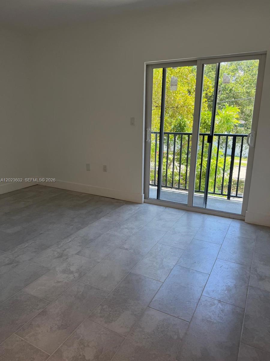An empty room features light gray tile flooring and a sliding glass door to a balcony — 147 Nw 59th St # 306, Miami FL 33127, MIAMI, FL