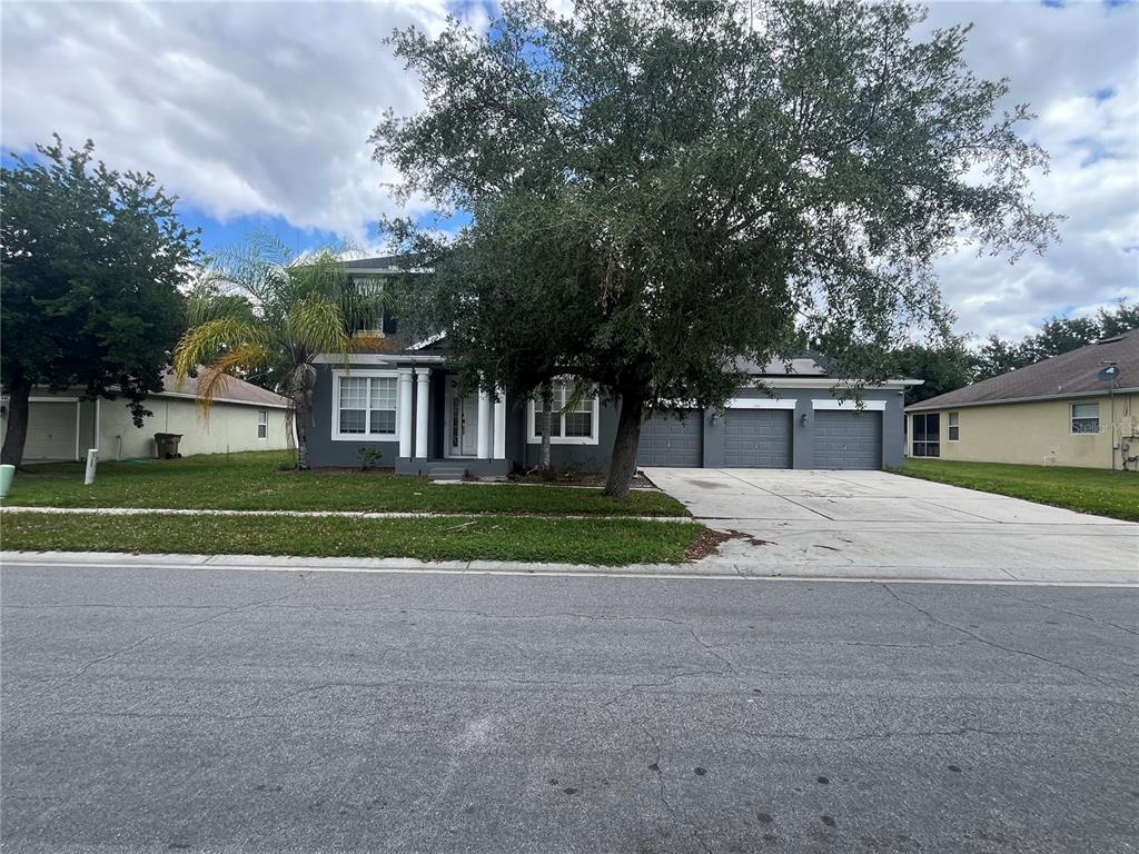A two-story gray house with a three-car garage and a large tree in front — 2981 MARSHFIELD PRESERVE WAY, KISSIMMEE, FL