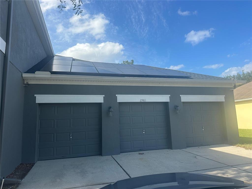 A three-car garage with solar panels on the roof under a blue sky — 2981 MARSHFIELD PRESERVE WAY, KISSIMMEE, FL
