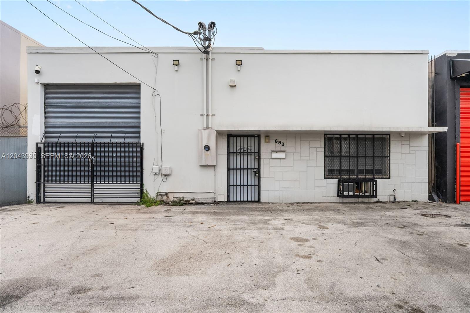 The exterior of a commercial building features a roll-up door, a gated entrance, and a window — 693 W 26th St, Hialeah FL 33010, HIALEAH, FL