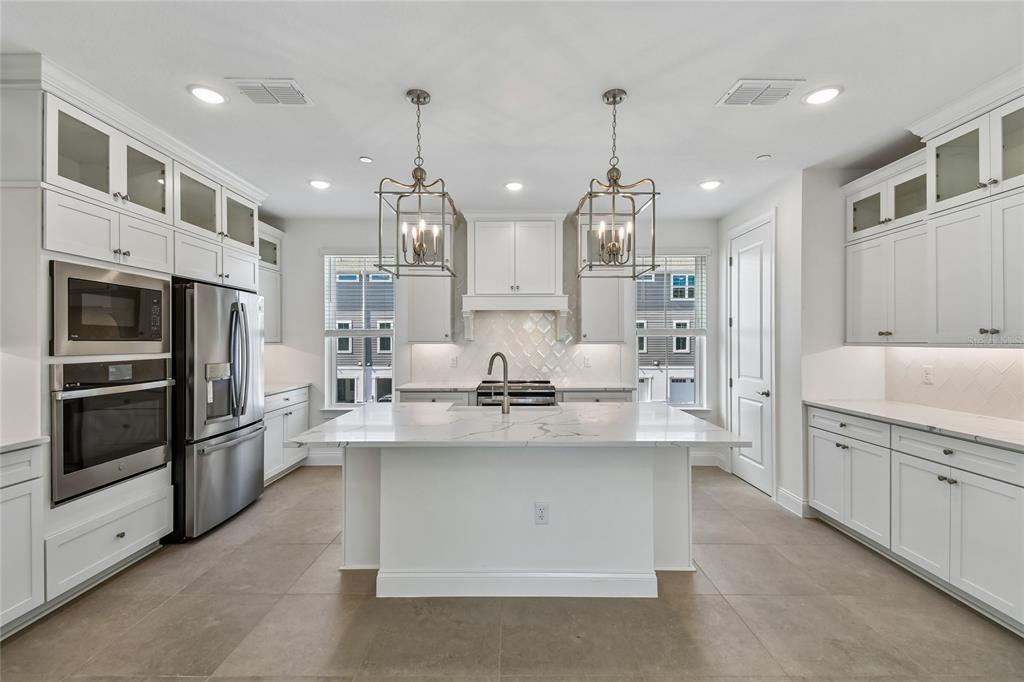 A modern white kitchen features a marble-topped island, stainless steel appliances, and two pendant lights — 222 PASQUALA, OVIEDO, FL