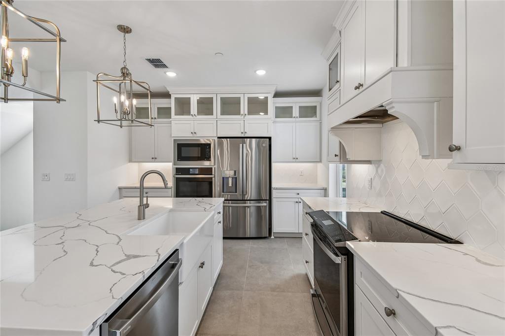 A modern kitchen features white cabinetry, quartz countertops, a farmhouse sink, and stainless steel appliances — 222 PASQUALA, OVIEDO, FL