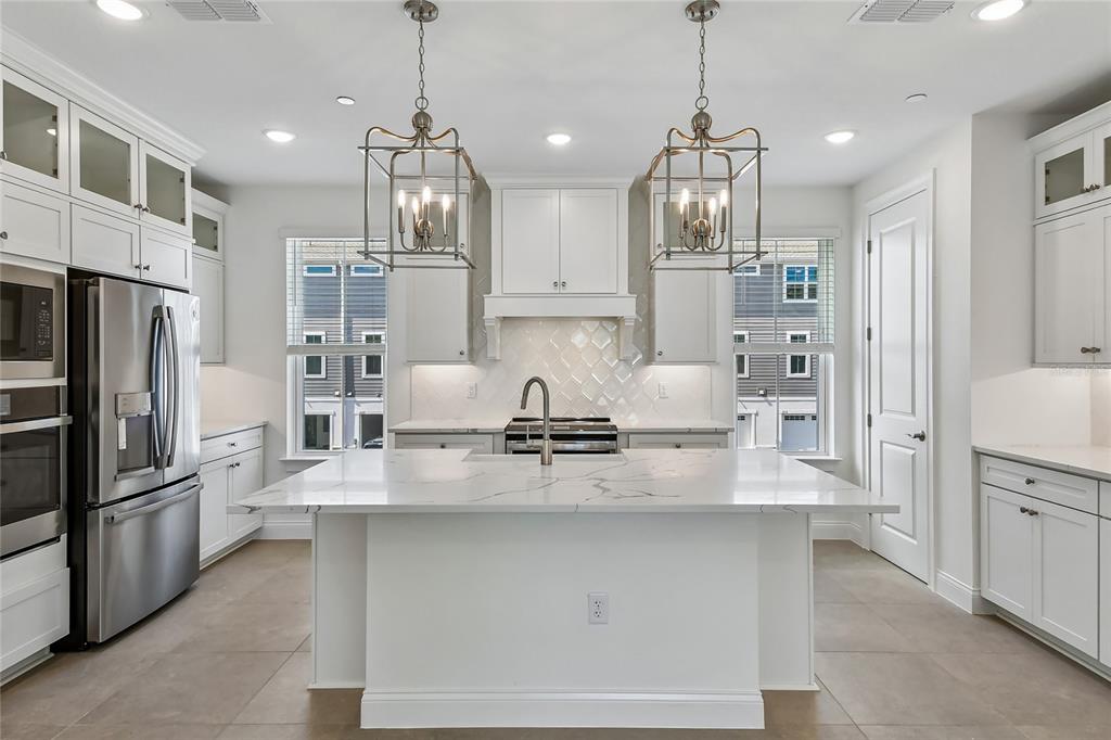 A modern white kitchen features a large marble-topped island, stainless steel appliances, and pendant lighting — 222 PASQUALA, OVIEDO, FL