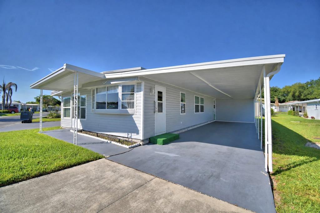 A single-story manufactured home with light gray siding, a large carport, and a concrete driveway — 117 HOLIDAY LANE, AUBURNDALE, FL
