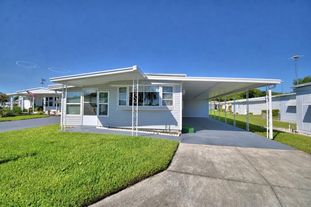 A light-colored mobile home features a large attached carport and a front lawn — 117 HOLIDAY LANE, AUBURNDALE, FL